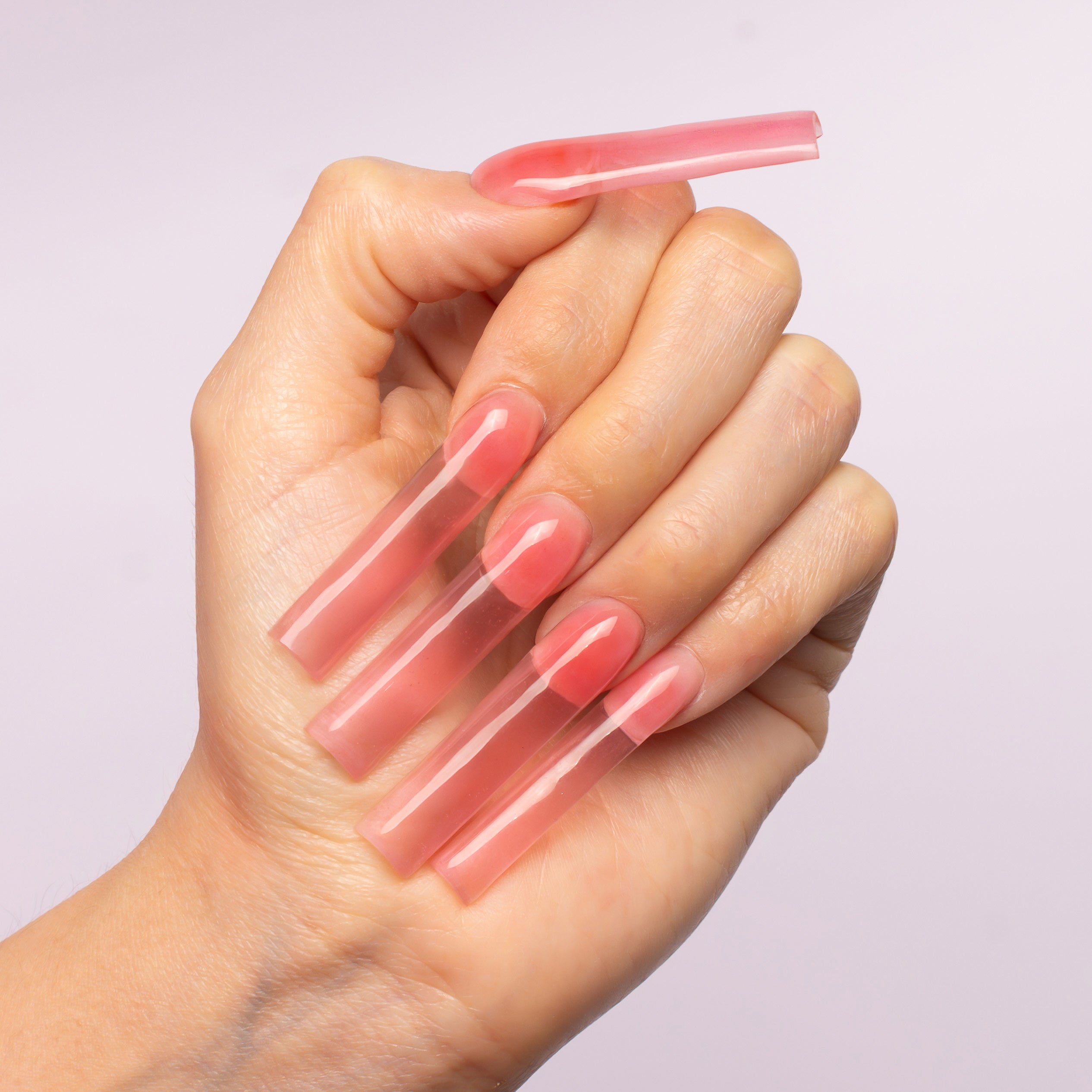 Hand holding a pink acrylic nail tool against a light purple background